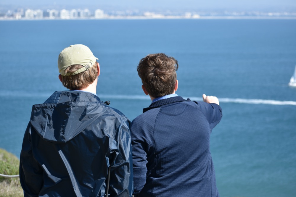 A view from the backs of Wyler and Ryan as Ryan points at something out of view across the harbor