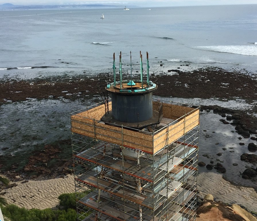 A fantastic view from a drone camera, at low tide, the lantern (top two sections of the tower) disassembly has begun. The upper lens room is now removed, leaving the barrel of the watchroom in view. (Photo by Ryan Strack.)