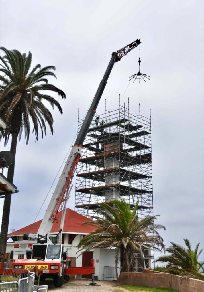 The crane was used for lifting 20,000 pounds of recast iron, piece by piece. Here, the roof frame is being lowered into place atop the lantern. (Photo by Kim Fahlen.)