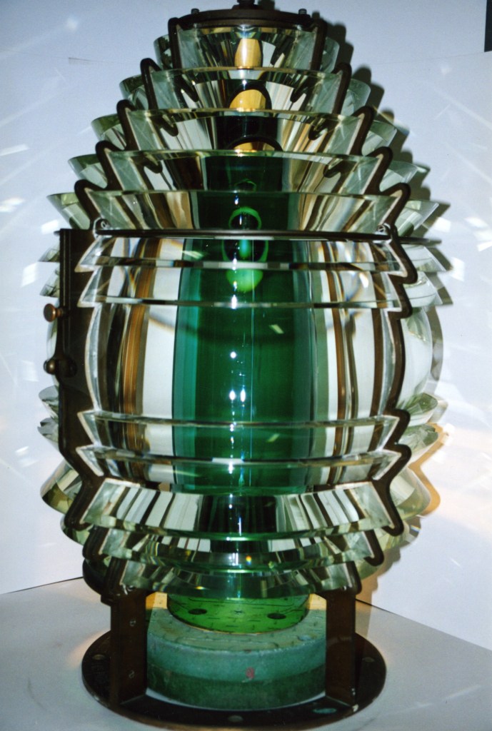 A large cylindrical light with a green center made from many pieces of small glass in different orientations focusing the beam of light.