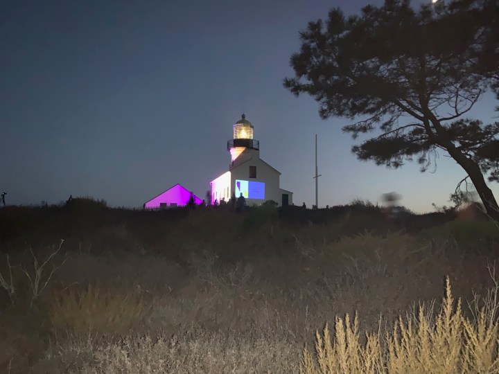 Lighthouse at night lit up with purple and gold with slideshow displayed on side of building.