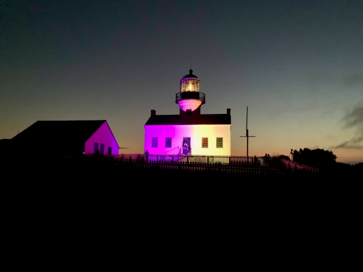 Lighthouse at night lit up with purple and gold.
