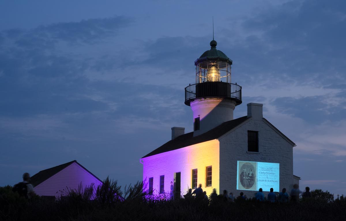 Lighthouse at night lit up with purple and gold with slideshow displayed on side of building.