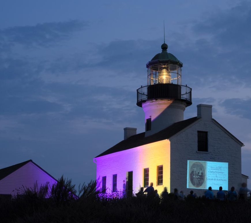 Lighthouse at night lit up with purple and gold with slideshow displayed on side of building.