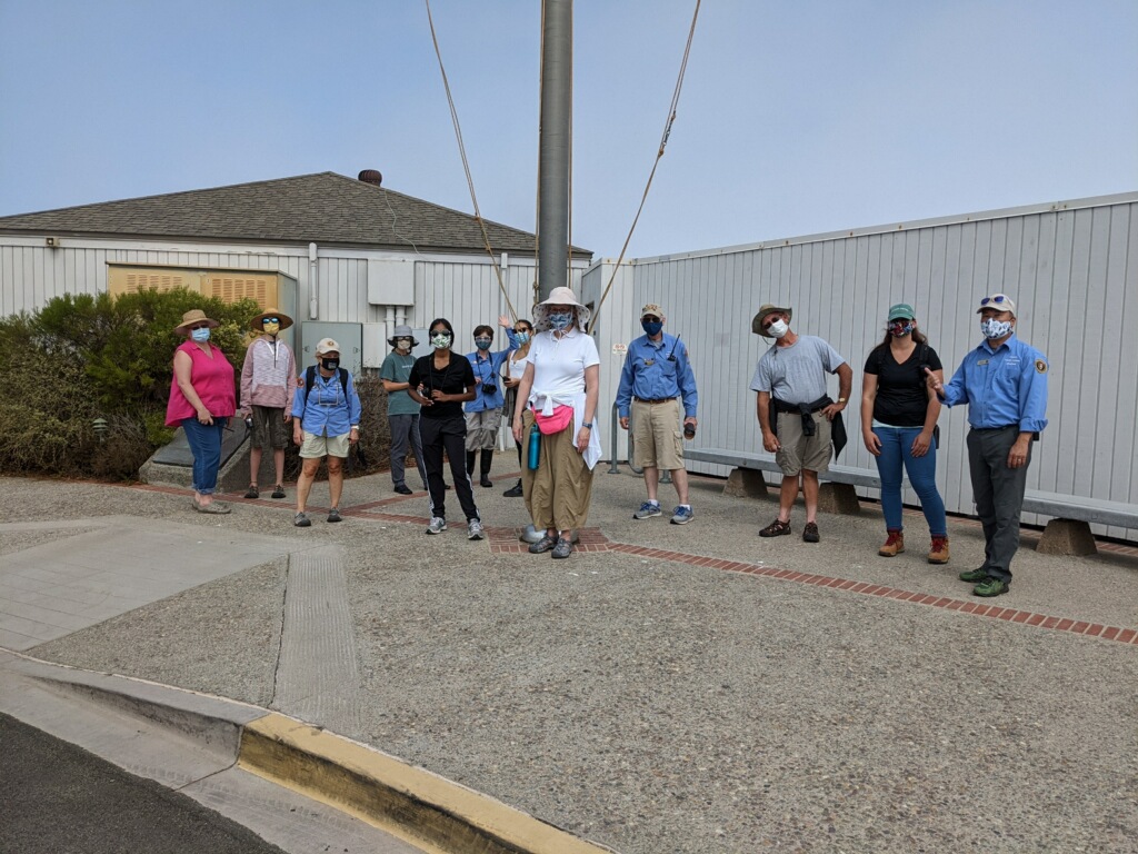 A group of men and women volunteers stand in front of a flag pole