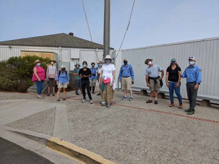 A group of men and women volunteers stand in front of a flag pole