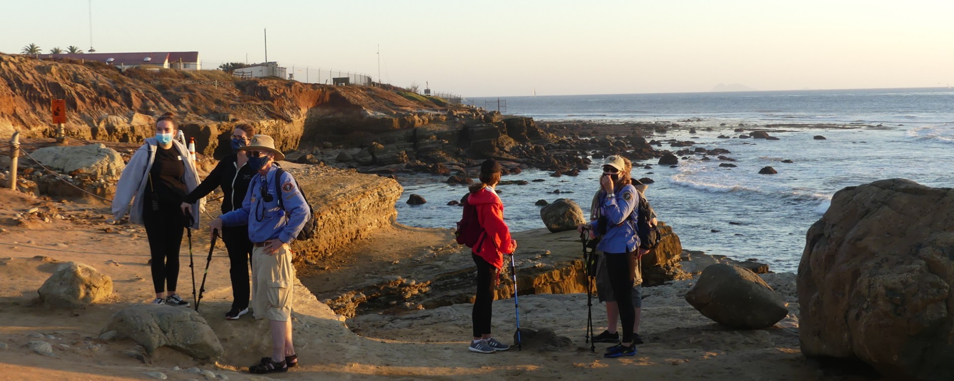People stand on sandstone cliffs overlooking the ocean. Volunteers are wearing long sleeve blue shirts.