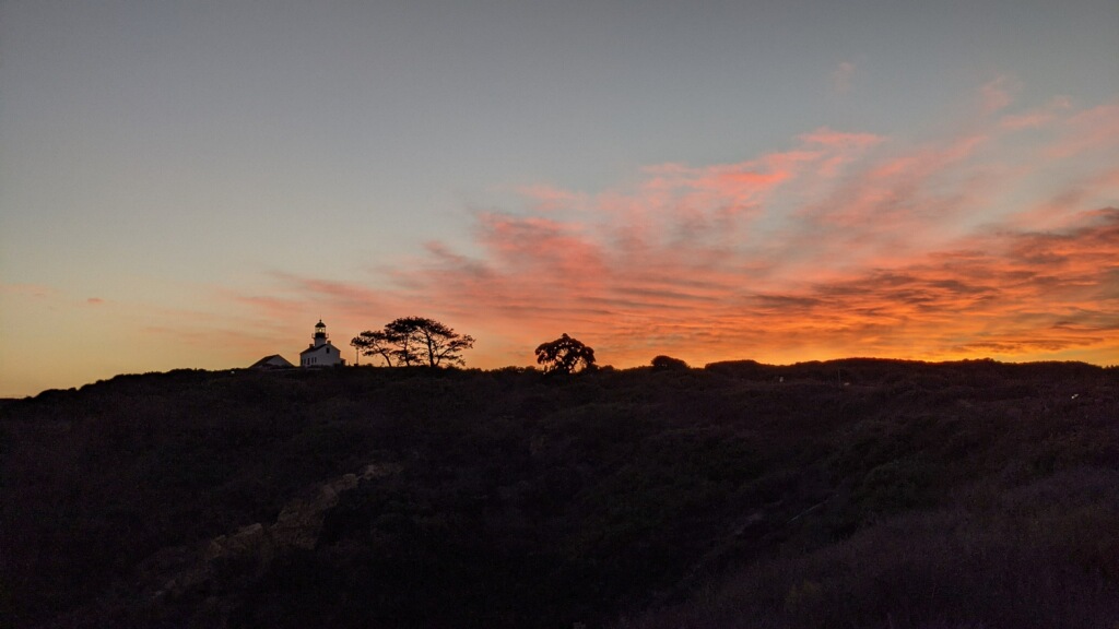 Panoramic orange sky at sunset with lighthouse and trees in shadow
