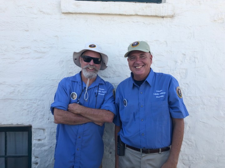 VIPs Craig (left) and Mike (right) smile and stand directly in front of a side of the Old Point Loma Lighthouse during an Open Tower Day event.