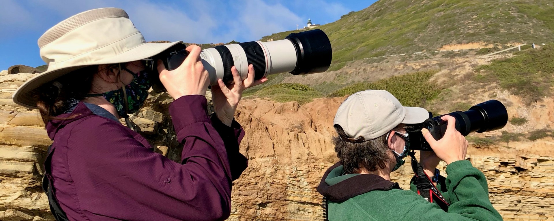 Two women holding cameras with long lens pointed at the sky, watching birds.