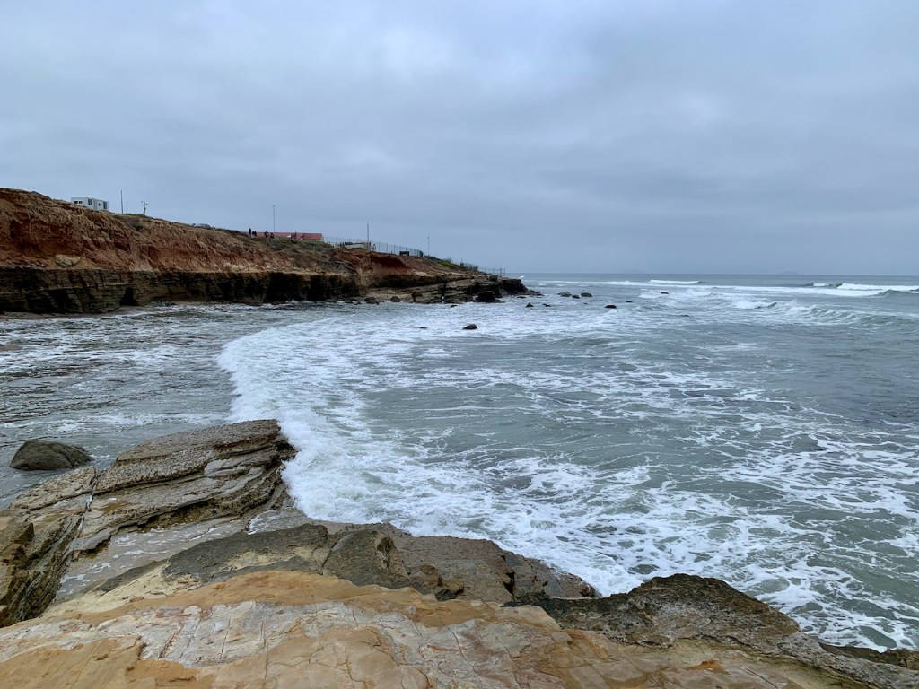 The ocean along a rocky cliff with a gray sky.