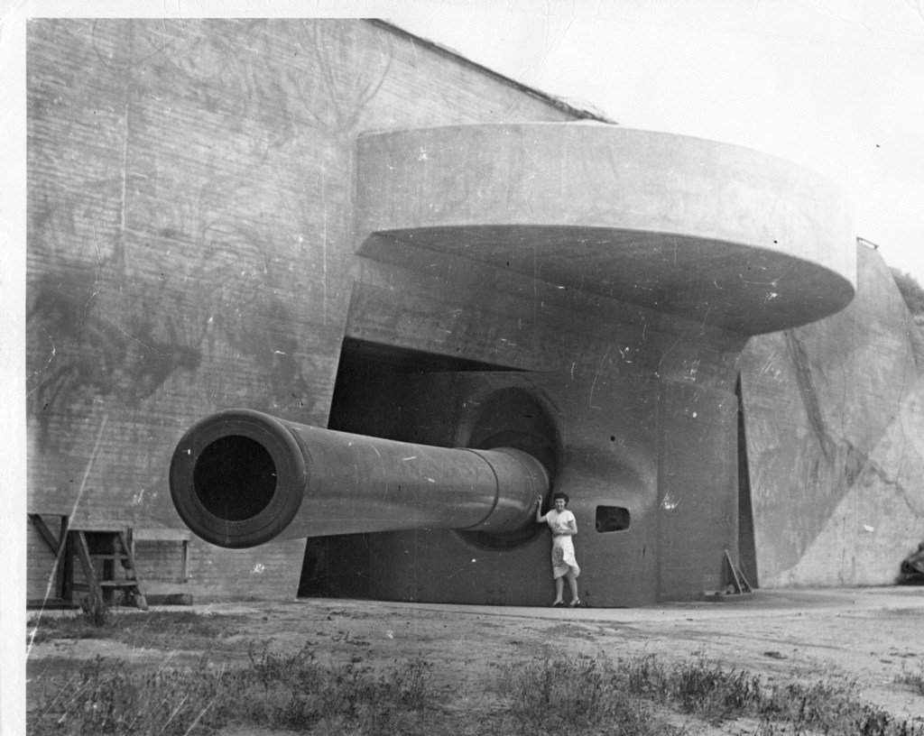 A woman stands next to a large cannon sticking out of a building.