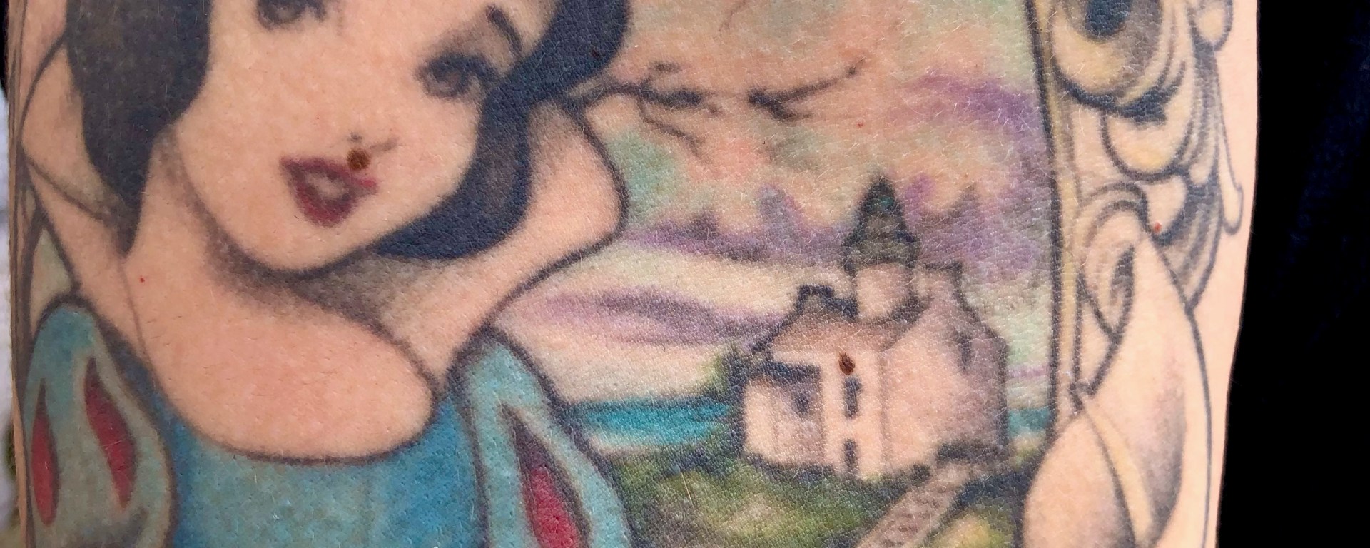 A tattoo on an arm showing a woman and a house inside an oval.