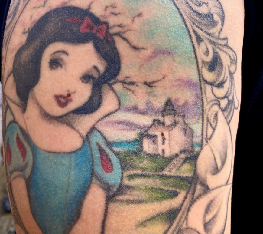 A tattoo on an arm showing a woman and a house inside an oval.