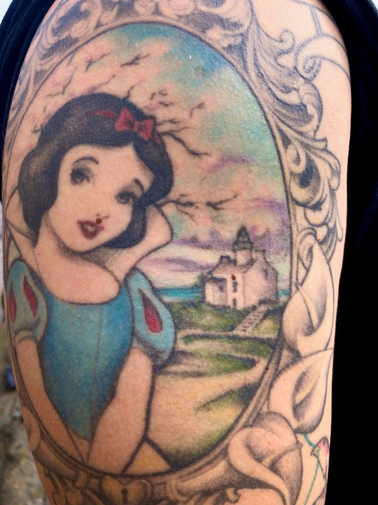 A tattoo on an arm showing a woman and a house inside an oval.