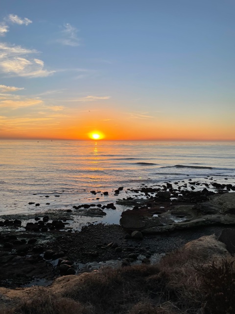 Sun sets in ocean with orange sky.