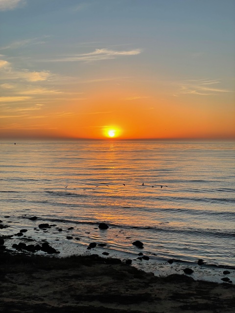 Sun sets in ocean with orange sky.