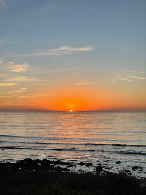 Sun sets in ocean with orange sky.