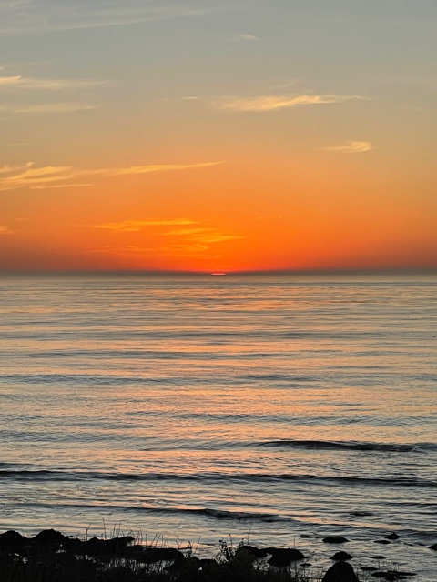 Sun sets in ocean with orange sky.