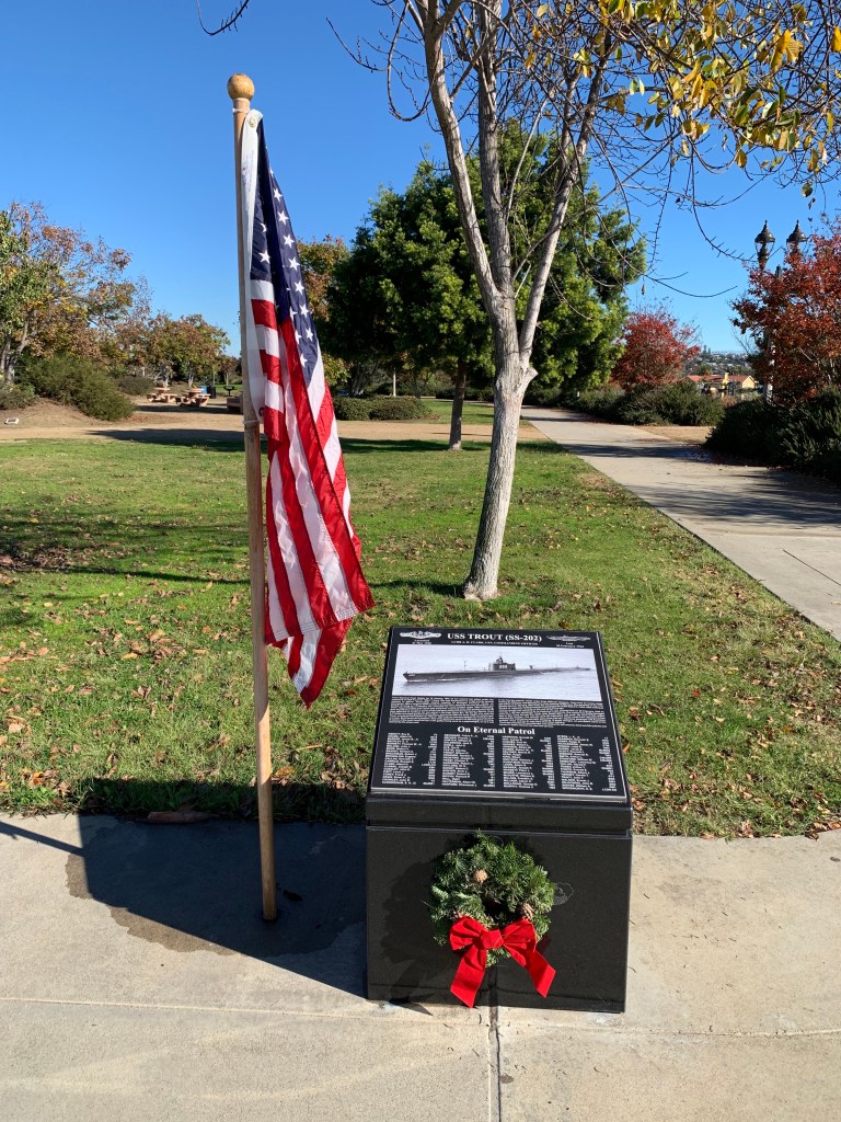 An American flag stands next to black memorial with wreath on front