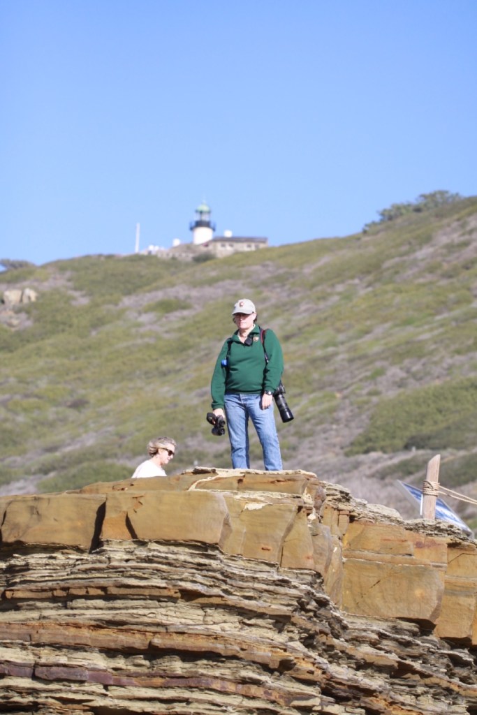 Woman in green jacket stands on top of rocky cliffs