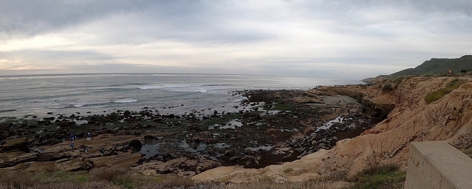 Tan sandstone cliffs along a rocky beach. Gray pillowy clouds cover the sky.