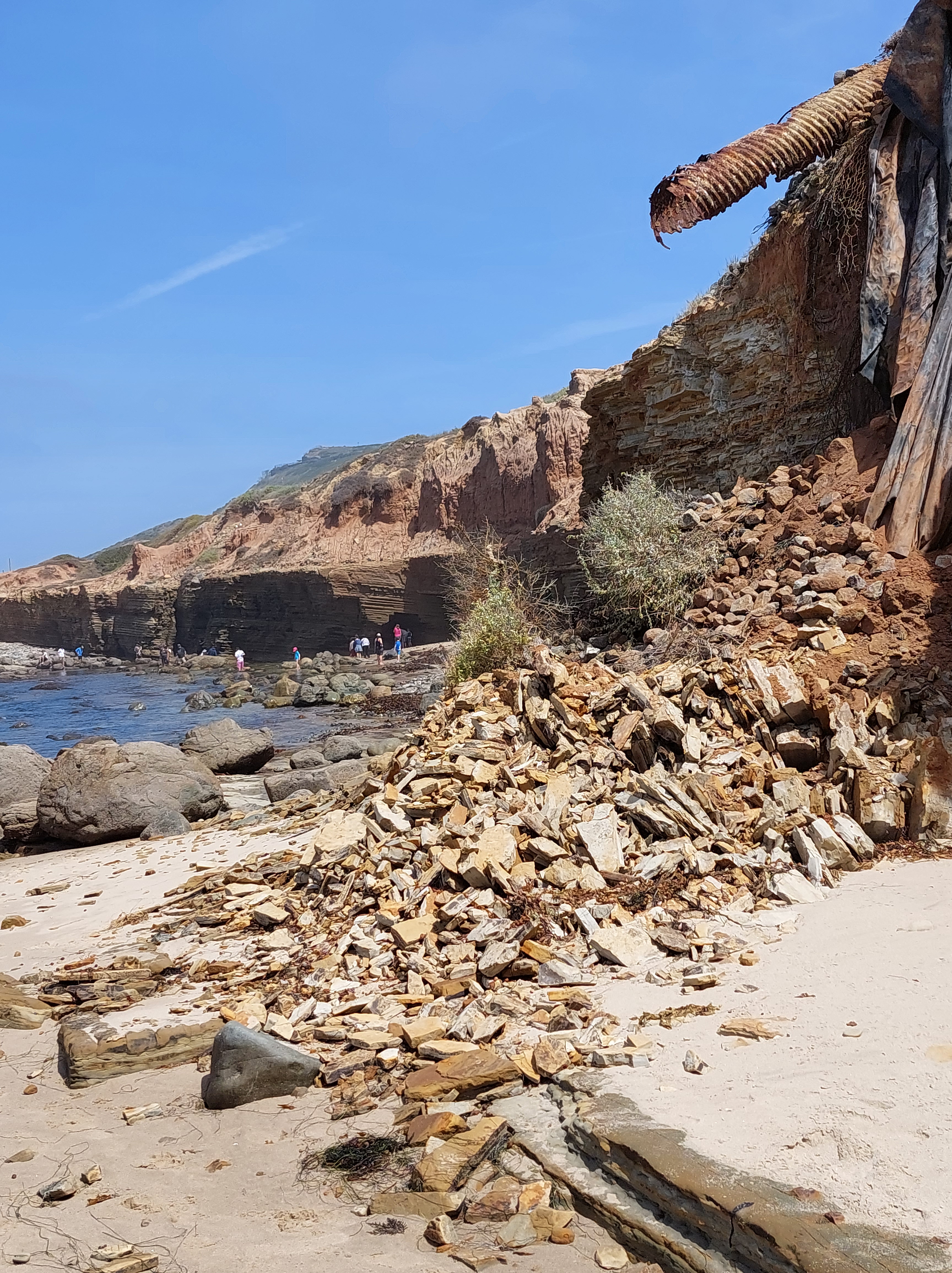 A pile of rocks that broke off from a cliff. A metal pipe sticks out from the cliff on the right side.