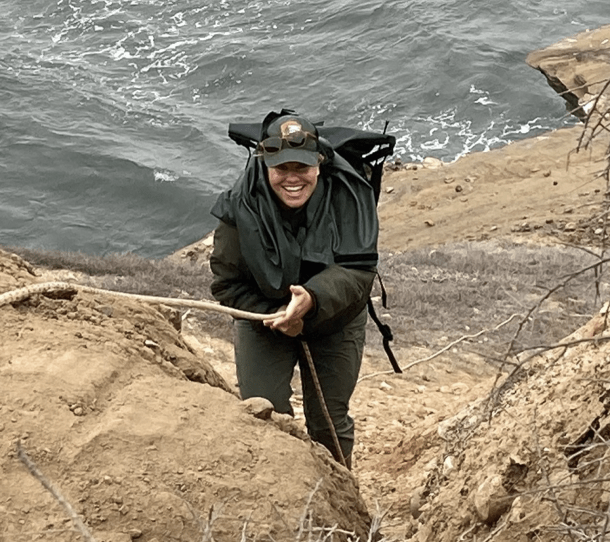 A woman climbing up a rope along a rocky cliff