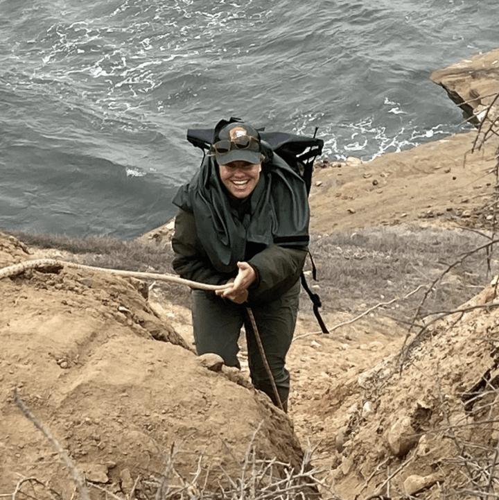 A woman climbing up a rope along a rocky cliff