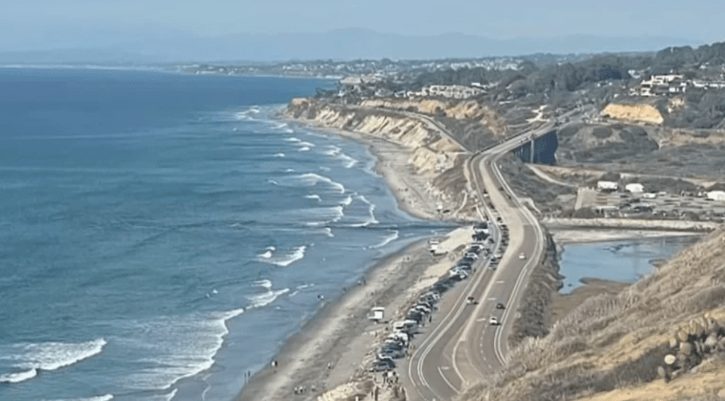 View from a cliff overlooking the ocean. A road parallels the ocean on the right.