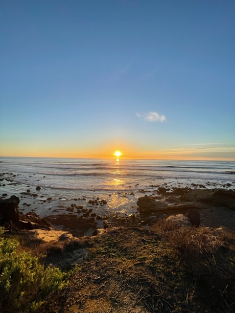 Sunset with a blue sky at the ocean. A rocky shoreline is in the foreground.