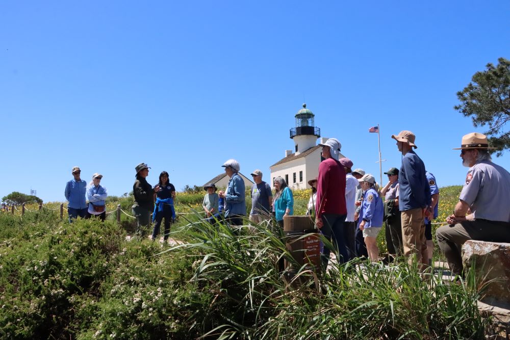 A group of people listen to a lady talking about flowers and plants.