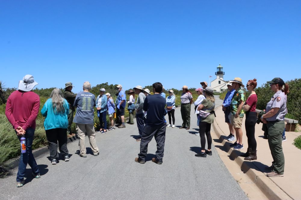 A group of people listen to a lady talking about flowers and plants.