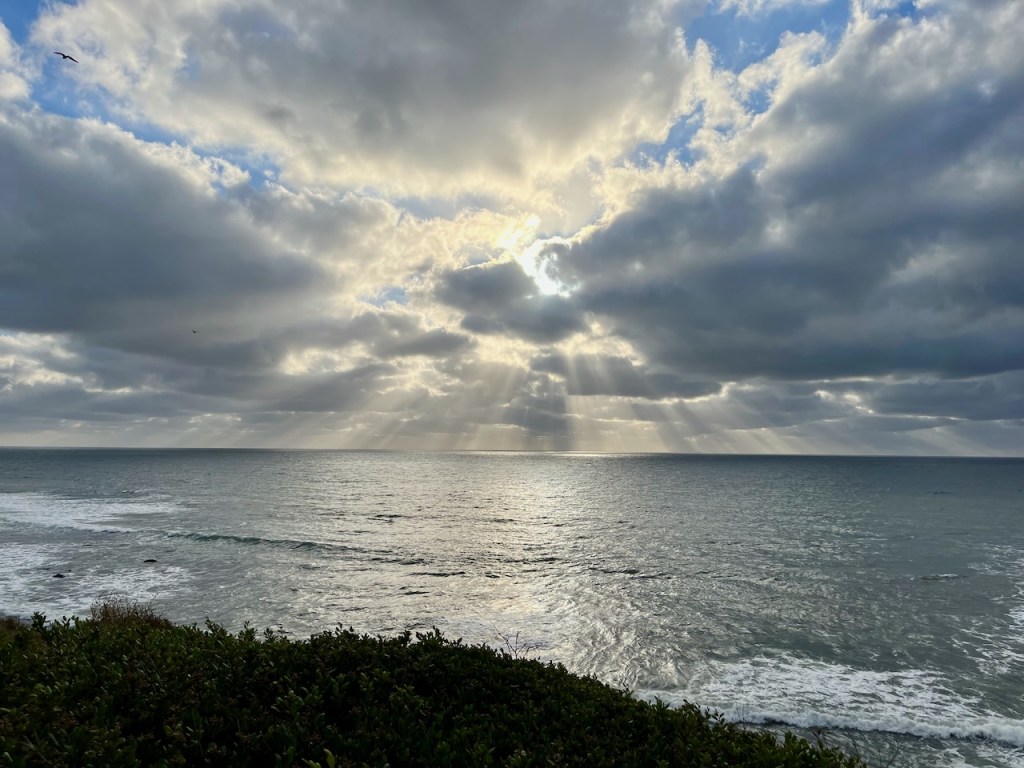 Sun poking through clouds along a rocky shore.