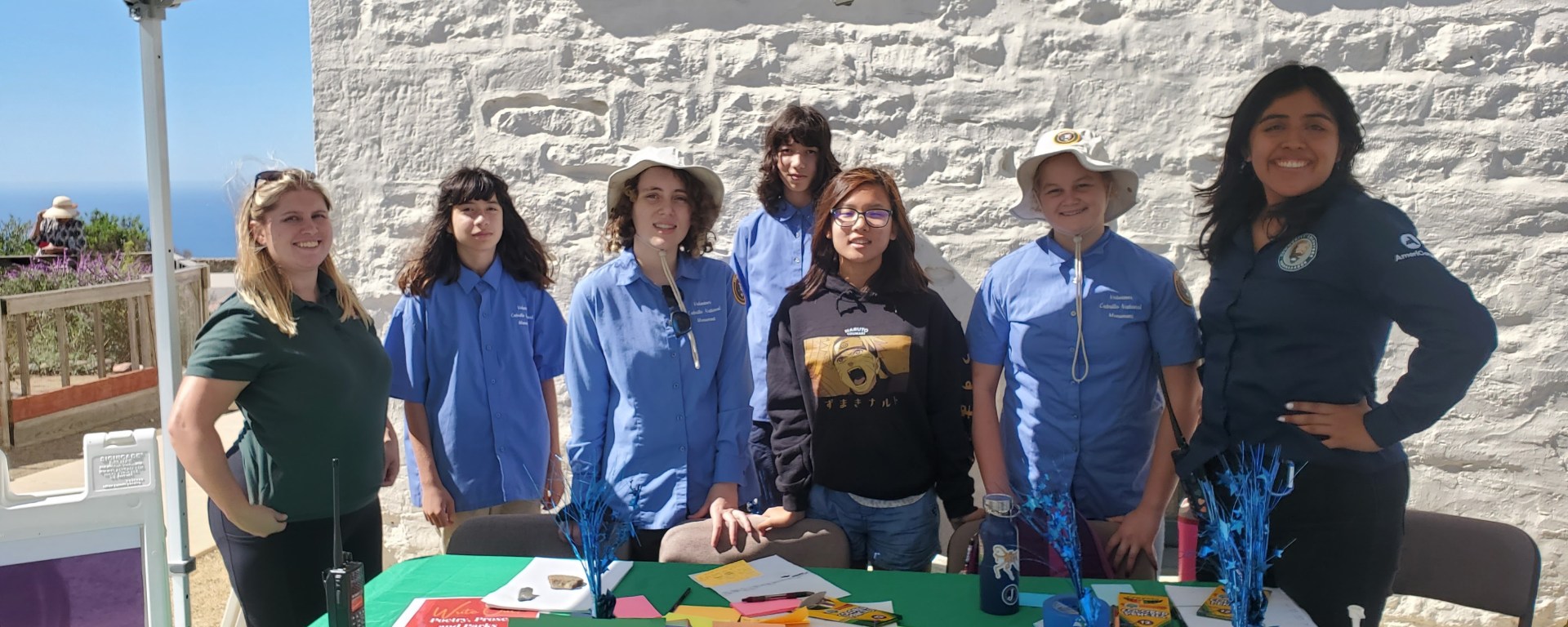 Five youth conservation and environmental stewardship apprentices and two park staff stand behind a table covered in various colored sticky notes and writing utensils, posing for a photo.