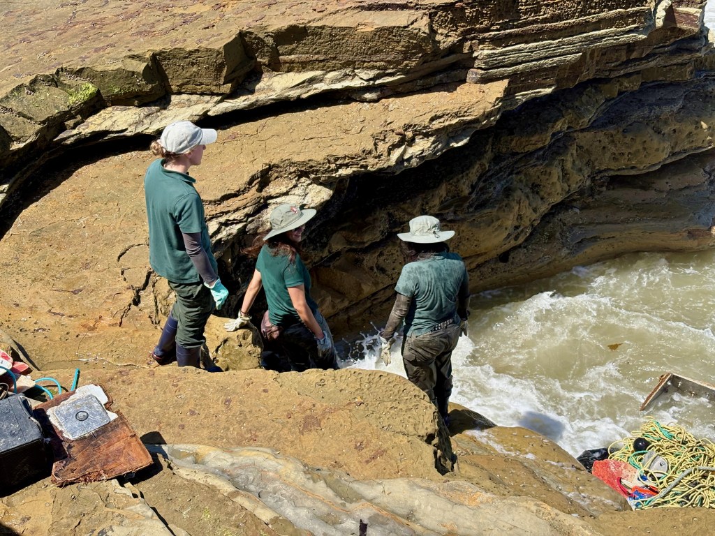 People in hats and gloves near a rocky shoreline with rushing water, possibly conducting research or exploration.