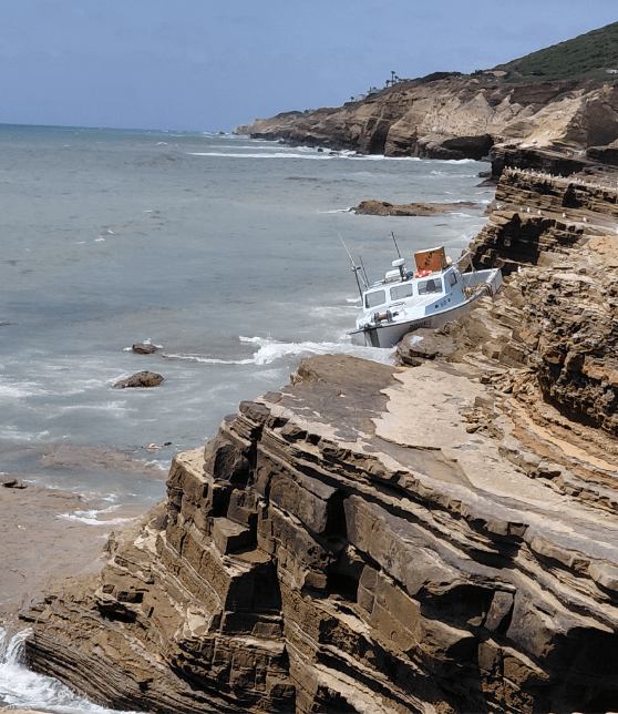 white boat stranded on rocky cliffs by the ocean, with waves crashing and seagulls perched nearby.