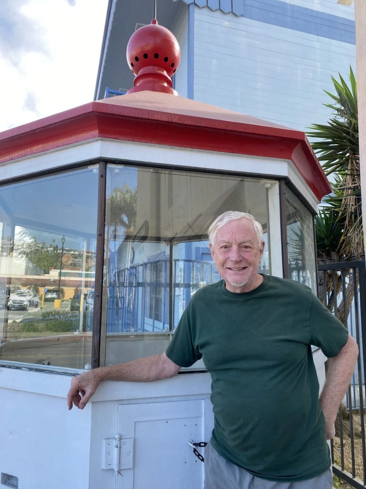 A man stands in front of a lighthouse lantern room.