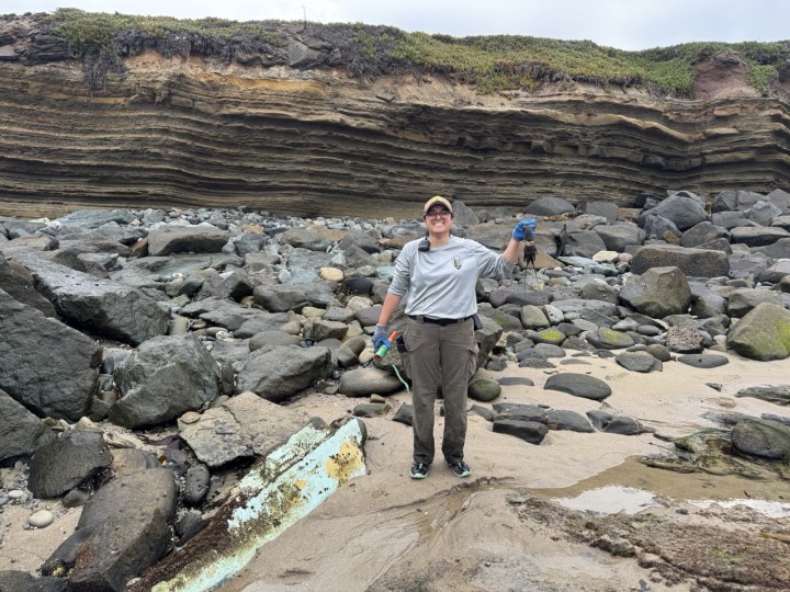 Woman stands on rocky shore holding lobster molt